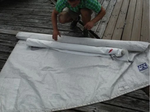 Sailor rolling the main sail around the jib