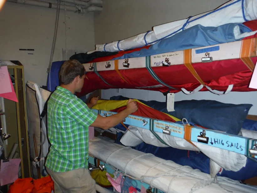 Sailor returning an FJ sail bag to its labeled shelf in the sail locker